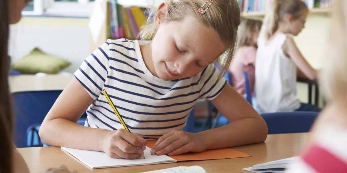 Een foto van een schoolgaand kind dat in een schrift schrijft